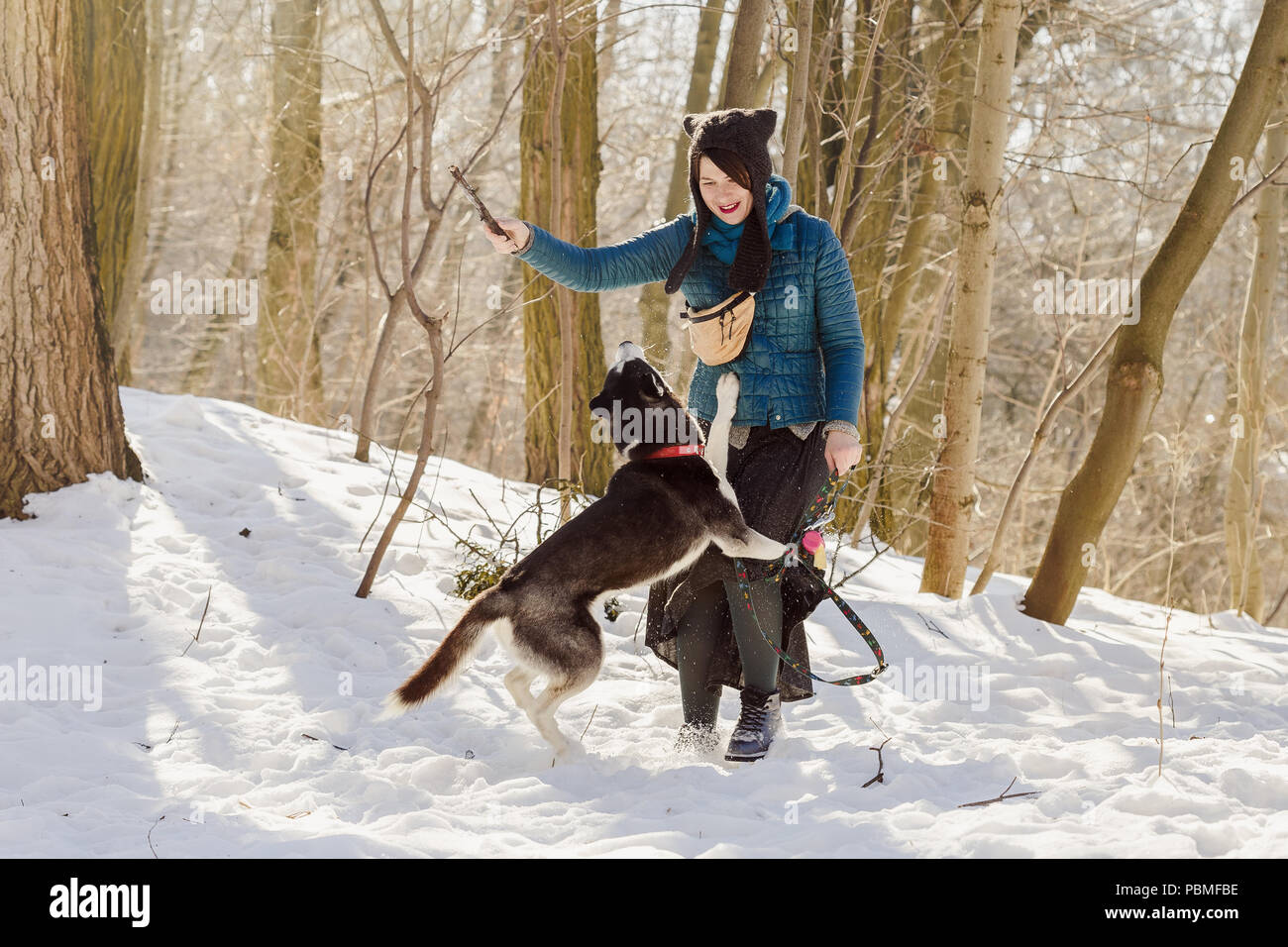 Mujer vistiendo elegante falda y sombrero divertido jugando con su perro  husky siberiano en el bosque de invierno con el palo Fotografía de stock -  Alamy