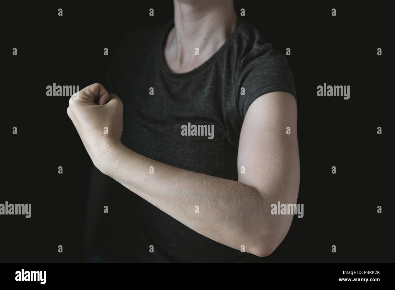 Imagen simbólica, el poder de la mujer, feminismo, mujer con tensa los músculos del brazo, fondo negro, foto de estudio Foto de stock