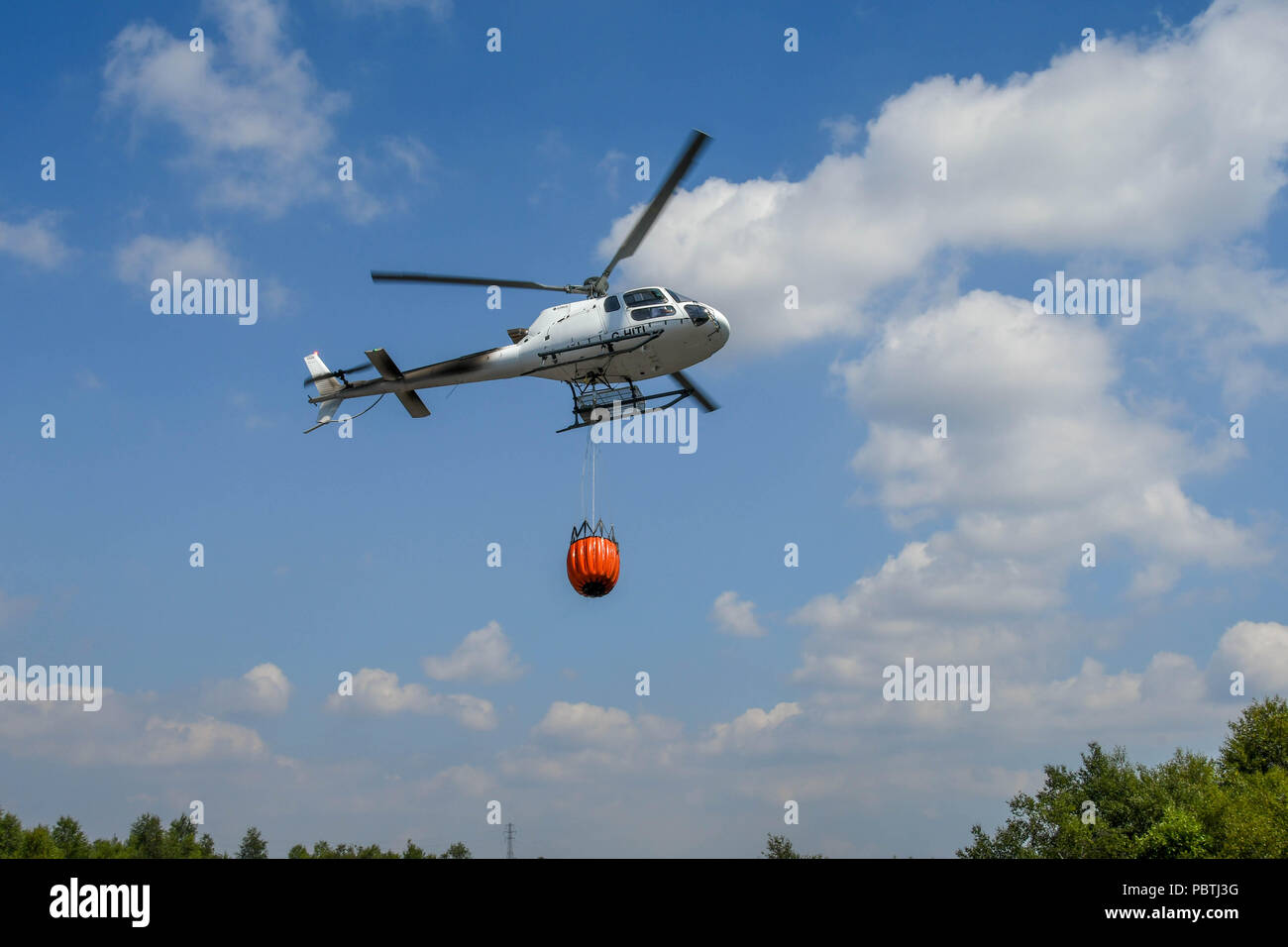 Un helicóptero que llevaba una gran cubo de agua. El helicóptero está siendo utilizada para combatir incendios de pasto. Foto de stock