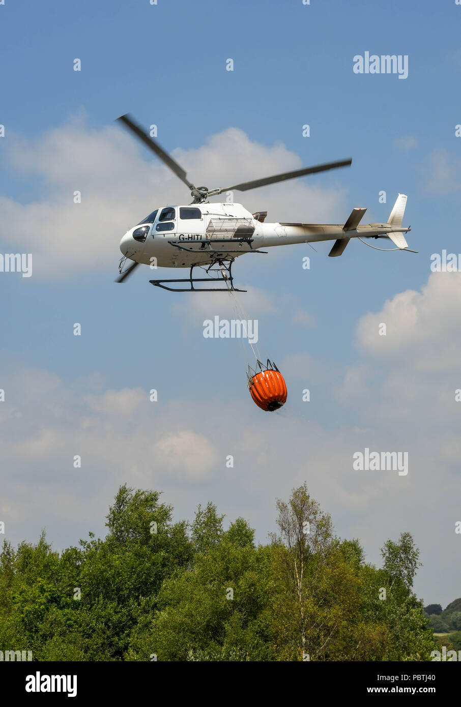 Un helicóptero que llevaba una gran cubo de agua. El helicóptero está siendo utilizada para combatir incendios de pasto. Foto de stock