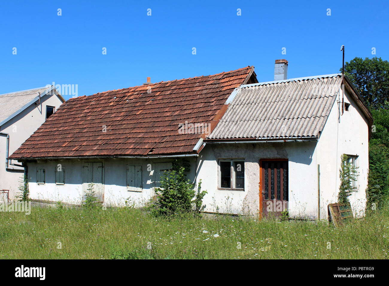 Muy pequeñas casas abandonadas con fachada ruinosas y tejas, puertas y  ventanas cubiertas con persianas de madera vieja rodeado con alta hierba  sin cortar Fotografía de stock - Alamy