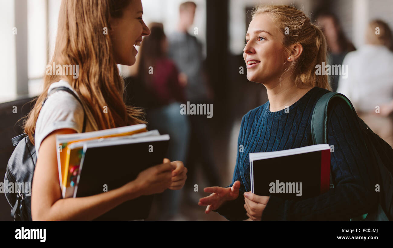 En la escuela secundaria de niñas sonrientes corredor. Dos mujeres estudiantes universitarios hablar después de la charla. Foto de stock