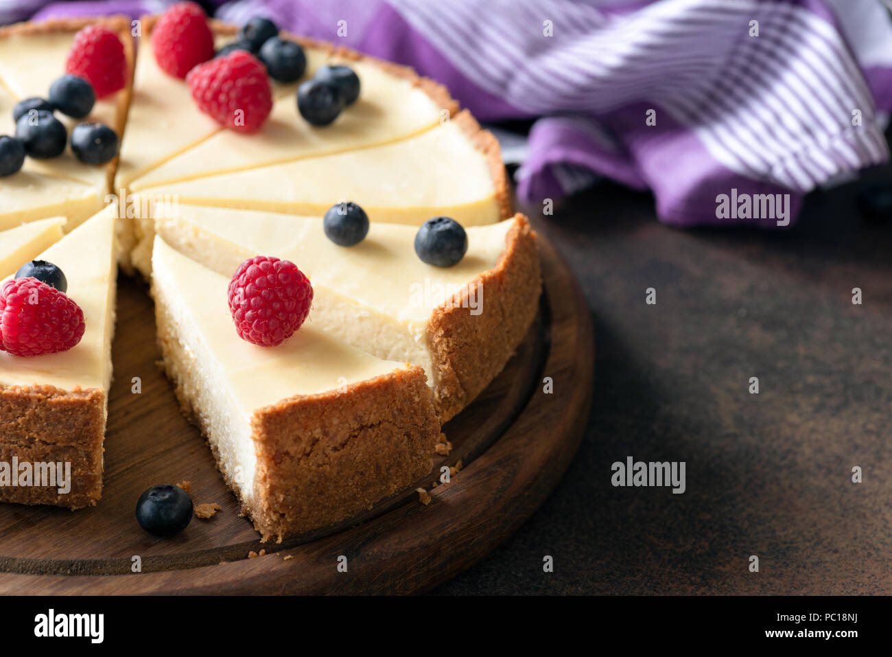 Classic plain New York Cheesecake con bayas frescas cortadas en madera, acercamiento, el enfoque selectivo Foto de stock