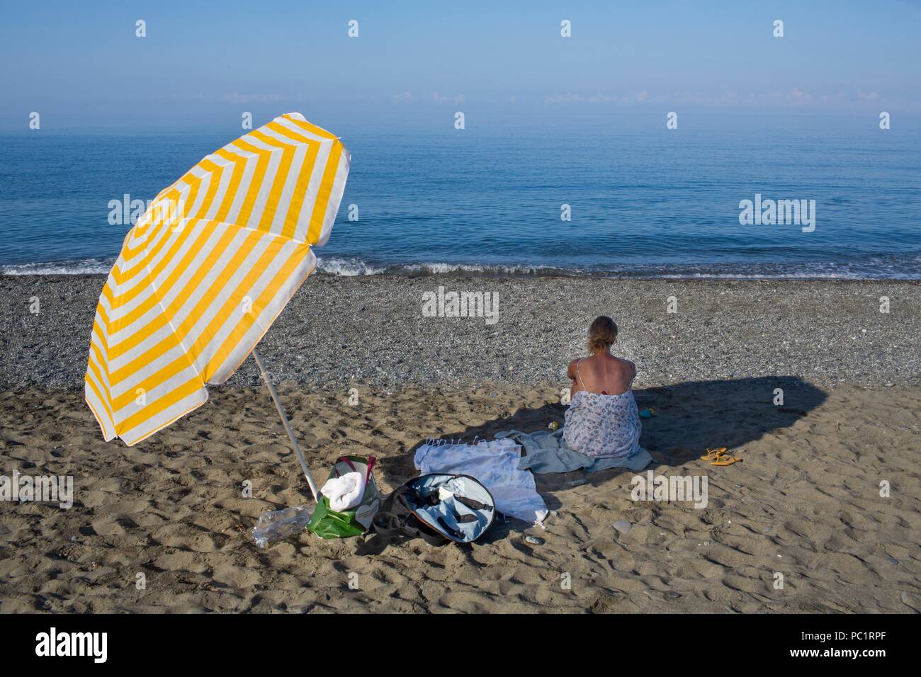 Mujer sentada en la sombra en la playa en Grecia Foto de stock