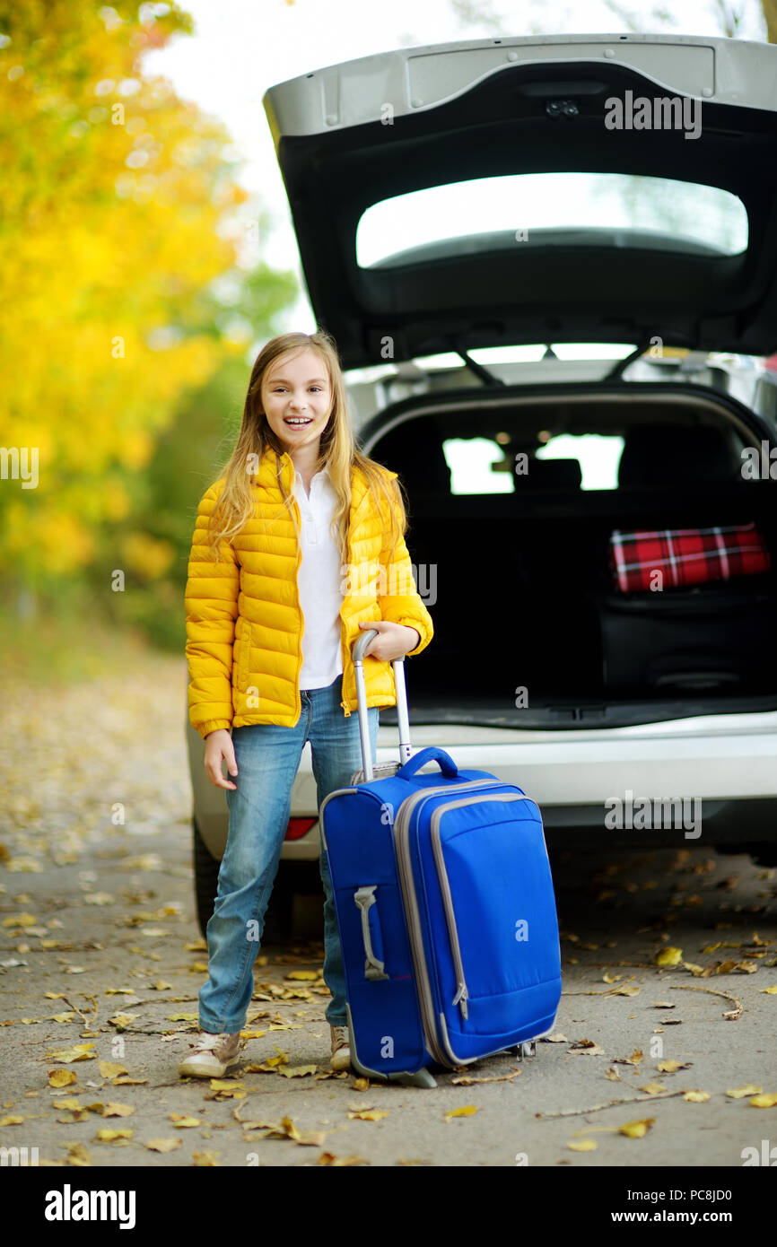 Adorable chica con una maleta lista para ir de vacaciones con sus padres.  Niño mirando hacia adelante para un viaje por carretera o viajes. Vacaciones  de otoño en la escuela. Actrav Fotografía