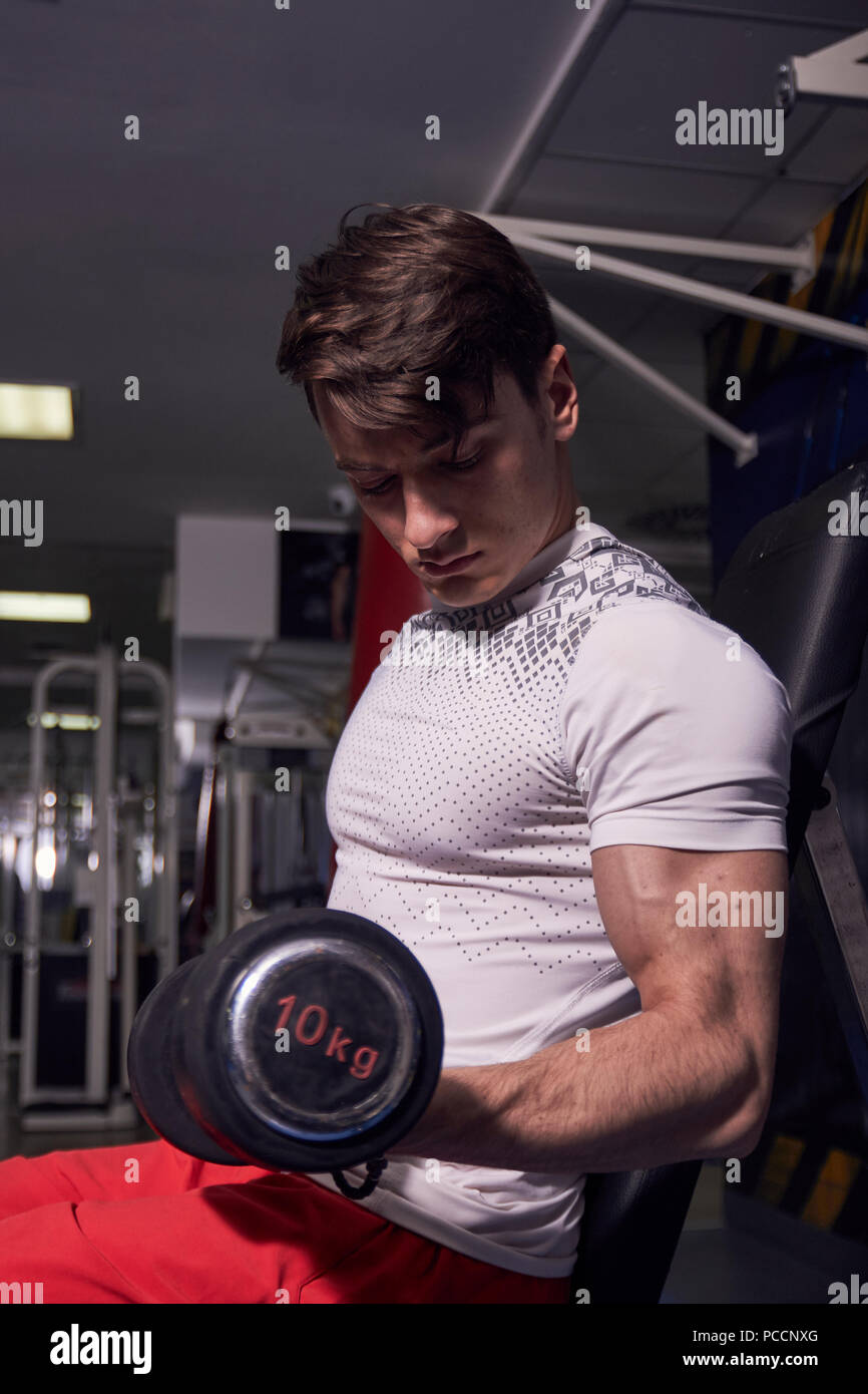 Un hombre joven, sosteniendo pesa ejercicio, bíceps brazo fuerte musculatura. vistiendo ropa deportiva. Vista lateral Foto de stock