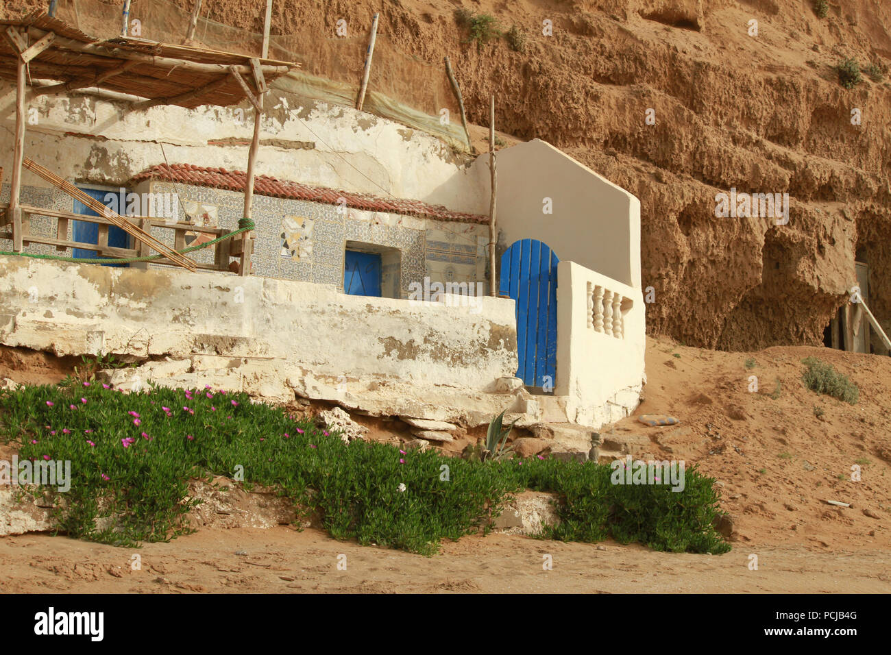 Las ruinas de la abandonada casa de pescadores con un pequeño jardín. Pueblo marroquí en la costa del Océano Atlántico. Foto de stock