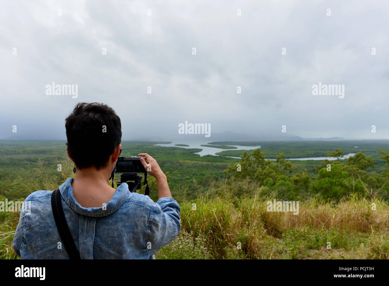 Una mujer mira a Hinchinbrook Island en un nublado día brumoso como se ve desde el mirador de la isla Hinchinbrook, Cardwell, Queensland, Australia Foto de stock