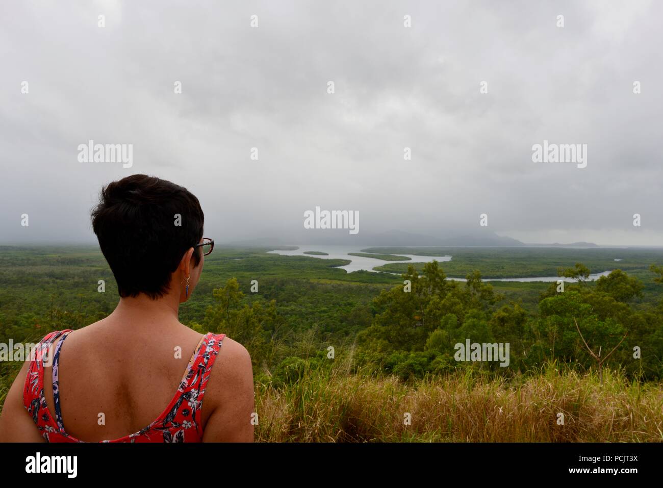 Una mujer mira a Hinchinbrook Island en un nublado día brumoso como se ve desde el mirador de la isla Hinchinbrook, Cardwell, Queensland, Australia Foto de stock