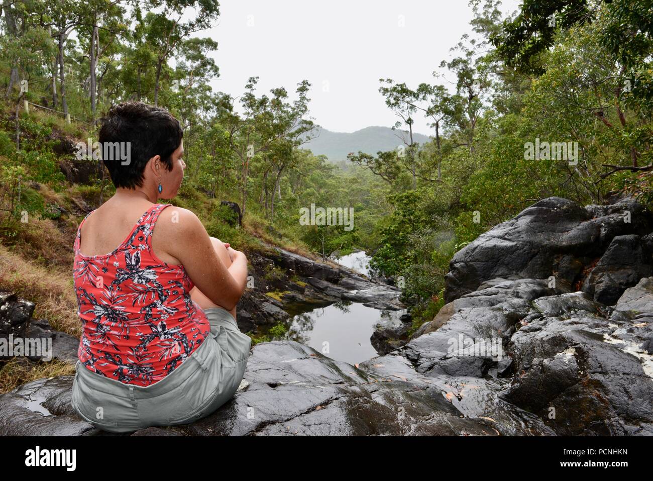 Una mujer sentarse y admirar las vistas al Creek Falls Attie Lookout, Cardwell, Queensland, Australia Foto de stock