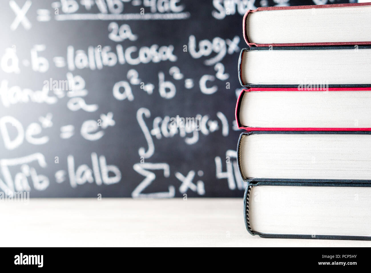 Pila y pila de libros delante de una pizarra en la escuela. Ecuación matemática escritos a mano en la pizarra. Foto de stock