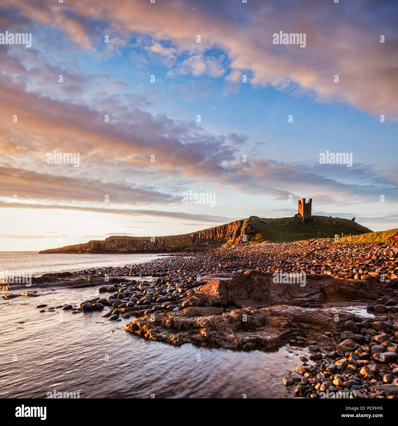 Castillo de Dunstanburgh, ahora una ruina, ordenando a la playa en la Bahía de Embleton, Northumberland, Inglaterra, bajo un espectacular amanecer. Foto de stock