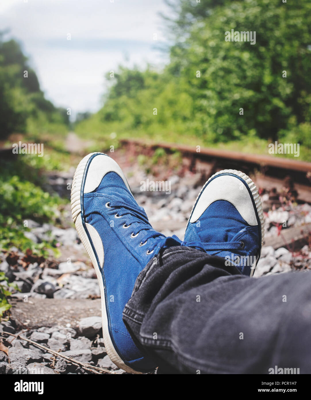 Hombre tumbado sobre un viejo, vías de ferrocarril, en negro jeans y zapatillas de lona azul de stock - Alamy