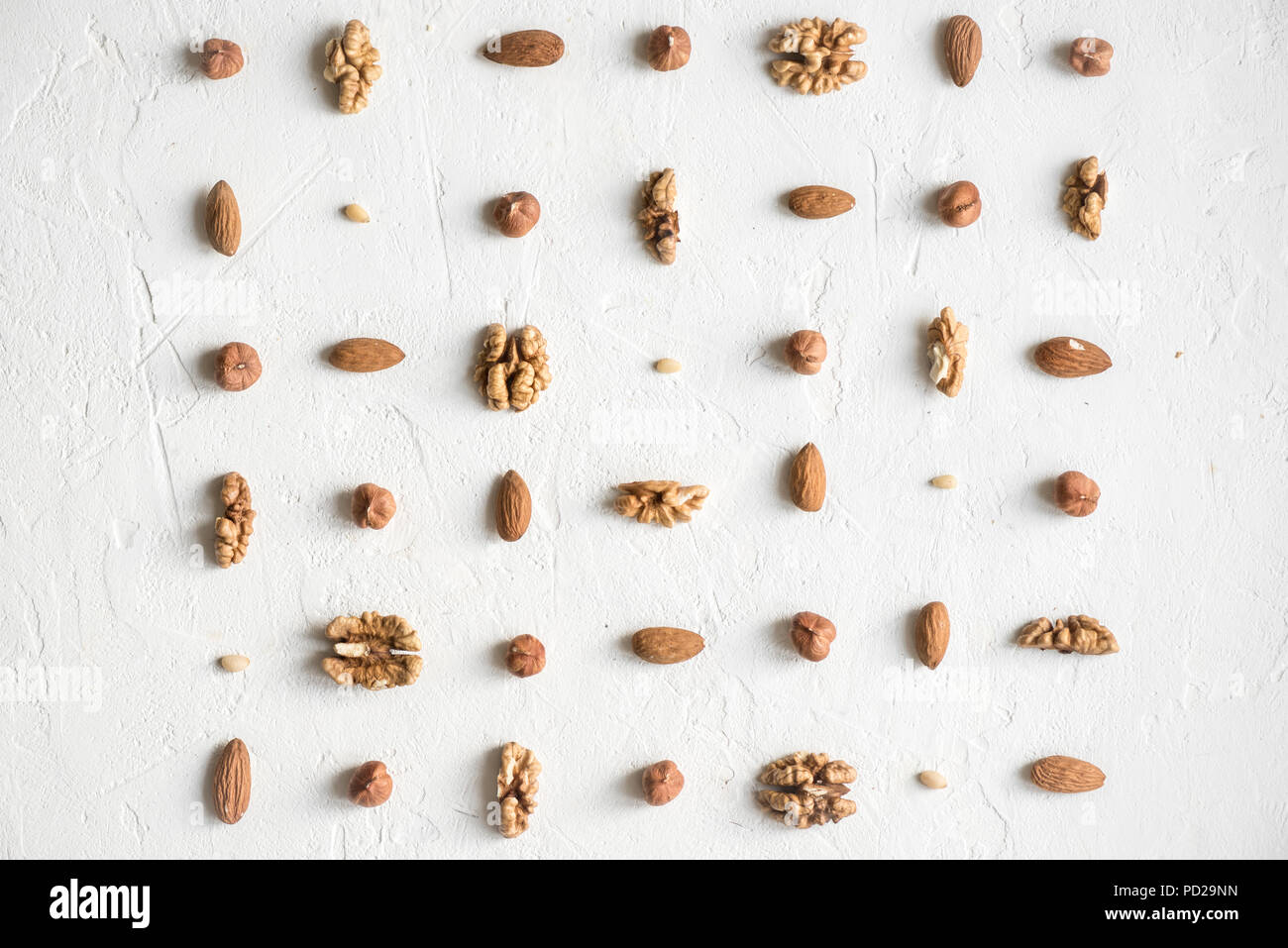 Diversos frutos secos (nueces, avellanas, almendras y piñones) repetición sobre fondo blanco como patrón, plana sentar con espacio de copia. Foto de stock