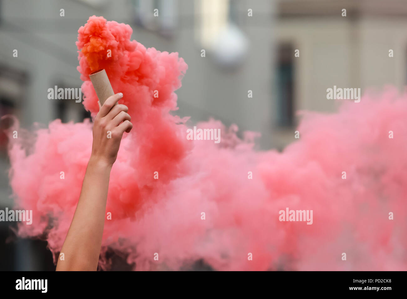 Un hombre sostiene una bengala de mano roja con humo. Foto de stock