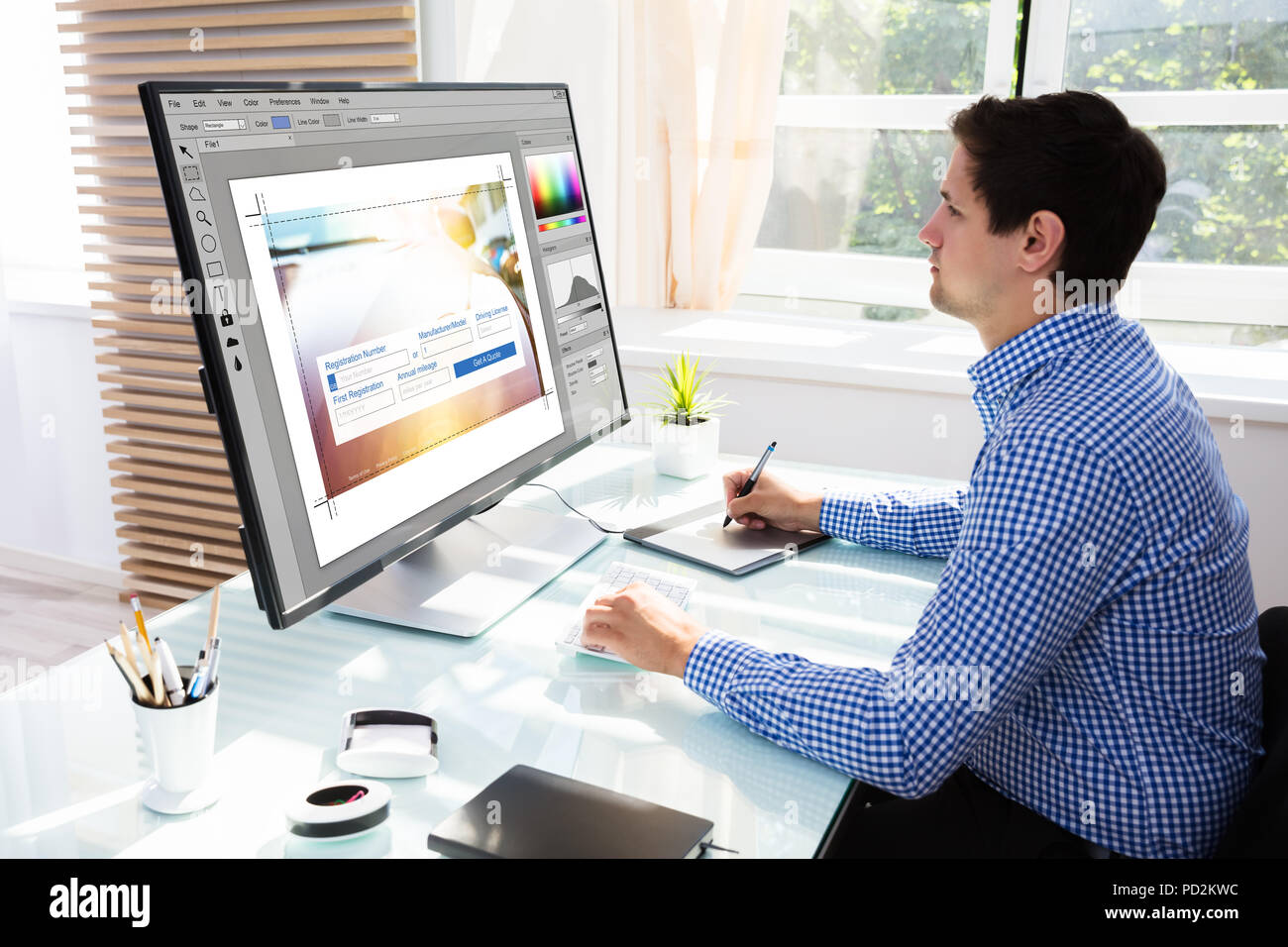 Macho joven editor utilizando tableta gráfica para el boceto mientras trabaja en equipo Foto de stock