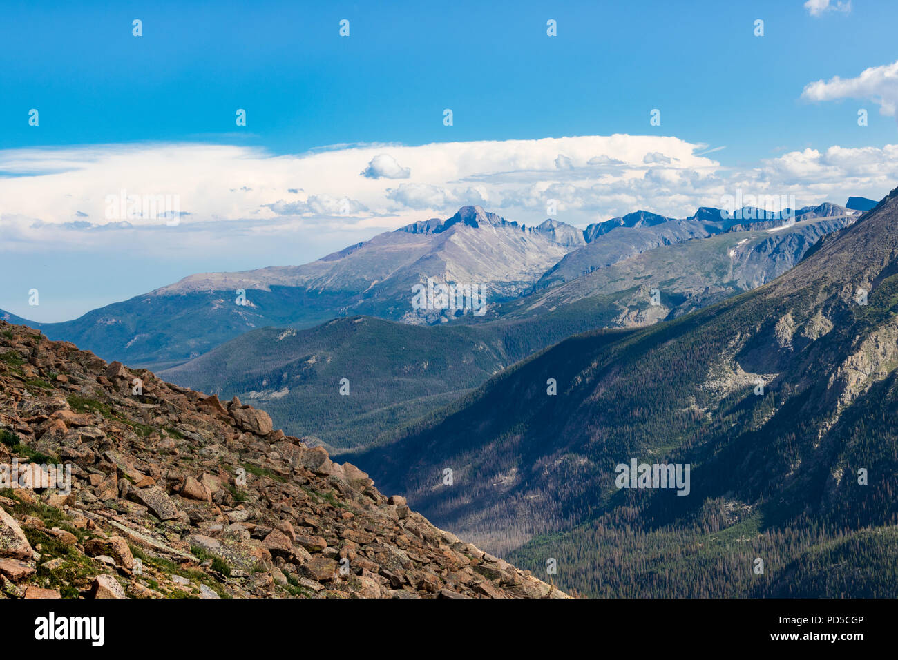 Colorado Rockies, soleado con Rocky Hill en delantero izquierdo de color azul-gris, espectaculares montañas detrás, con encinas de abajo. Cielo azul brillante y las nubes arriba Foto de stock