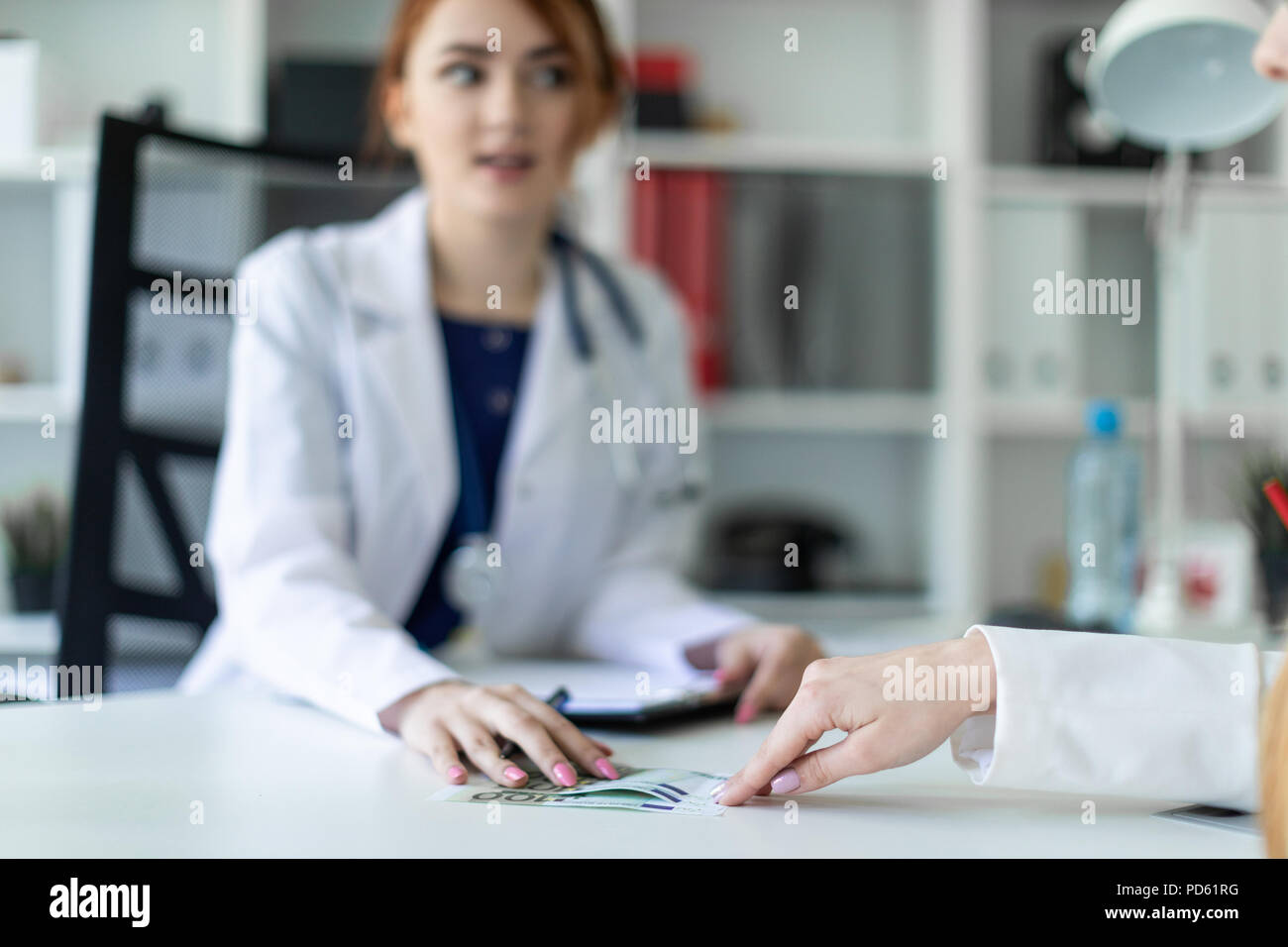 Una hermosa joven vestida con una túnica blanca está sentado en el escritorio de la oficina y la comunicación con el interlocutor. El interlocutor da la chica de dinero. Foto de stock
