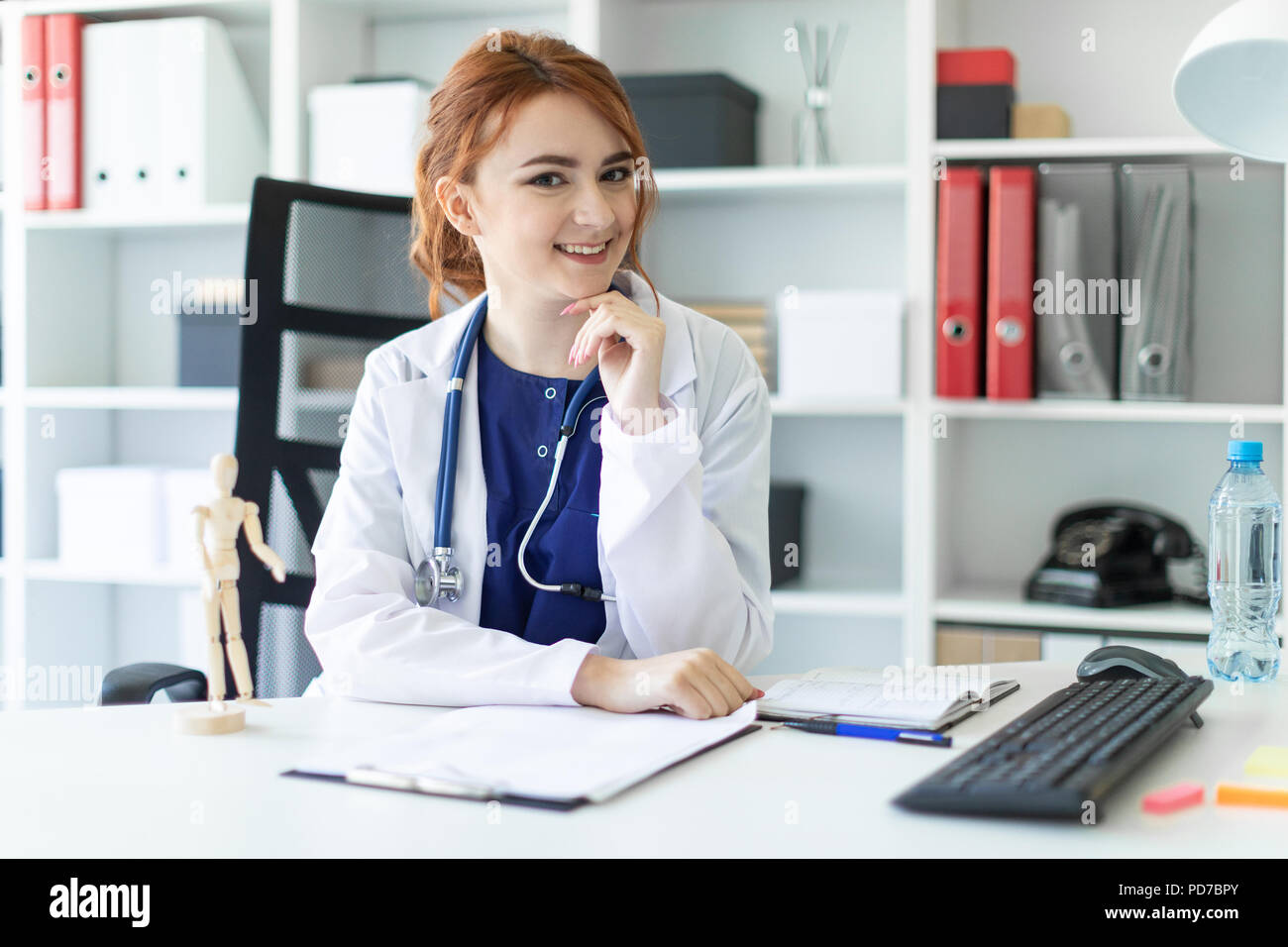 Una hermosa joven vestida con una túnica blanca está sentado en una mesa en la oficina. Foto de stock