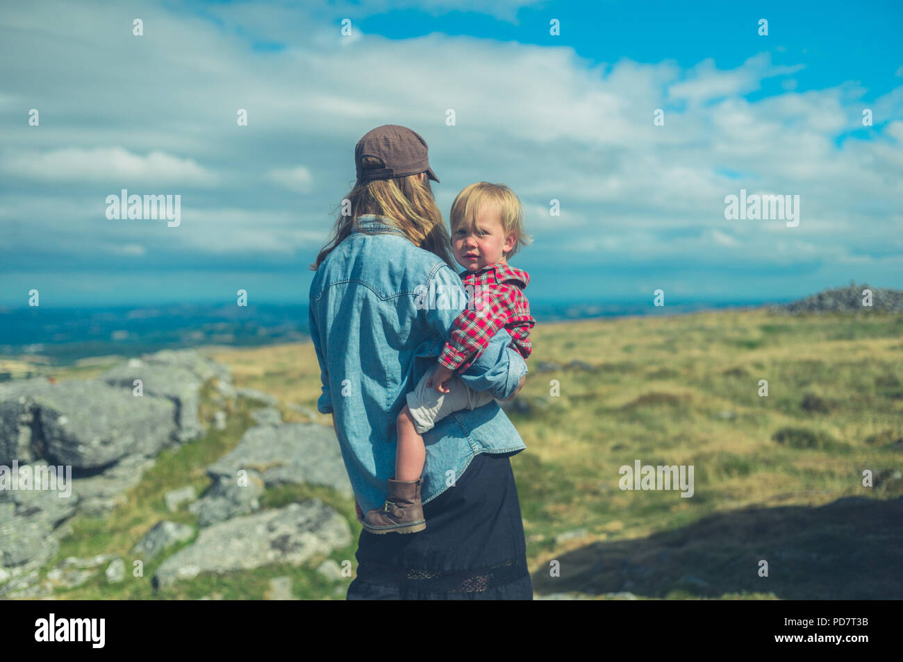 Una joven madre y su pequeño niño estén admirando la vista desde la cima de una roca en una colina en el páramo Foto de stock