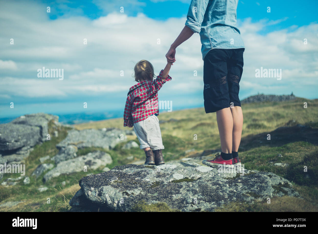 Una joven madre y su pequeño niño estén admirando la vista desde la cima de una roca en una colina en el páramo Foto de stock