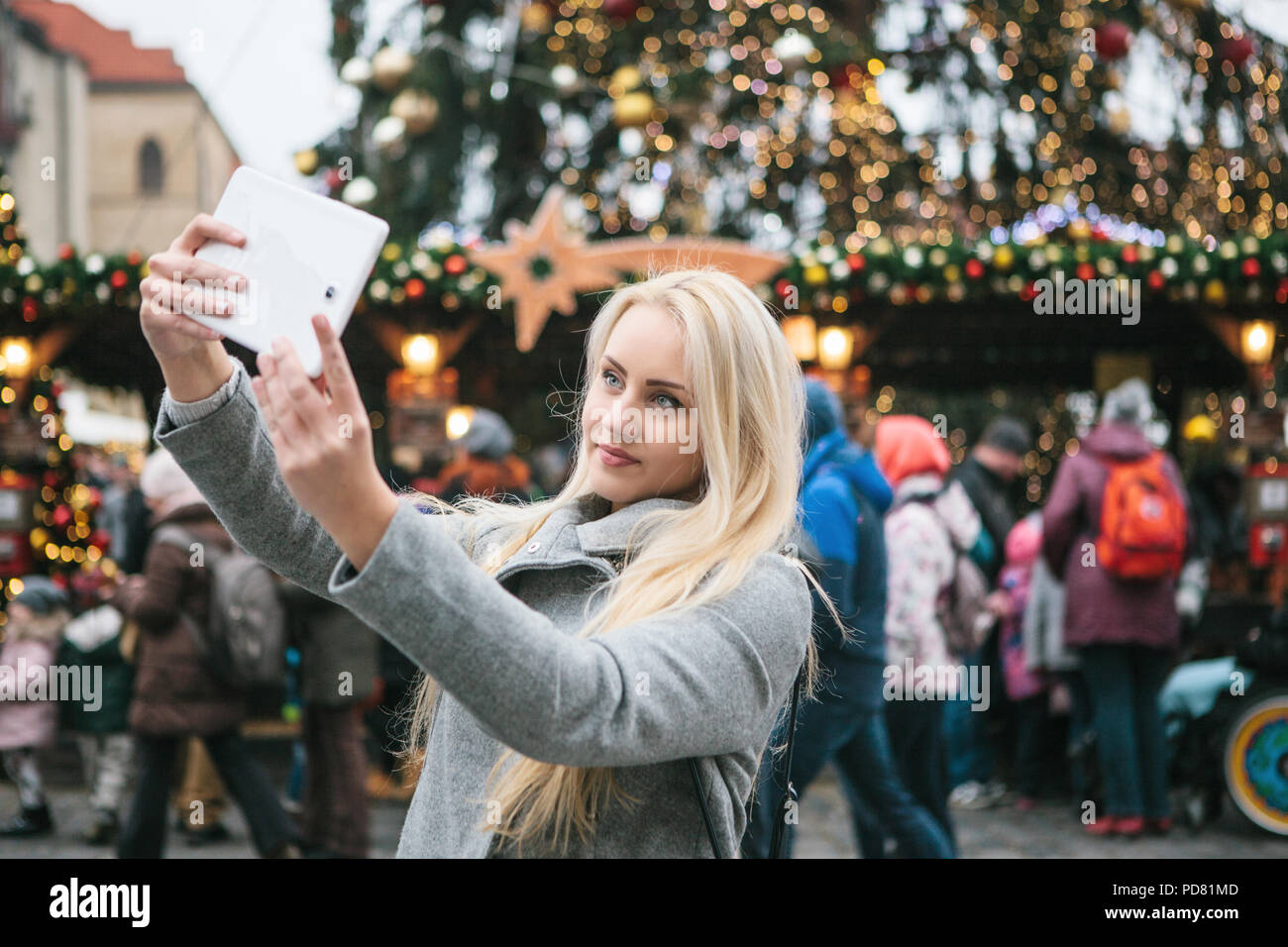 Una joven y bella mujer rubia o niña haciendo selfie o fotografiar junto a un árbol de Navidad durante las vacaciones de Navidad en la Plaza de la Ciudad Vieja en Praga, República Checa. Foto de stock