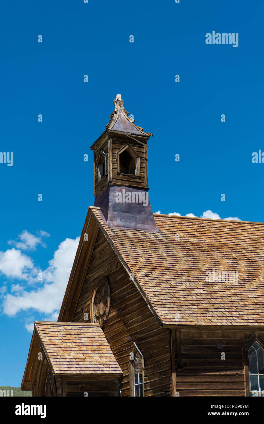 Abandonada de madera antigua iglesia y campanario bajo el hermoso cielo azul y las nubes hinchadas en la ciudad fantasma de Bodie, California Foto de stock