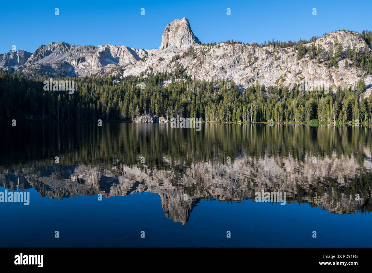 Reflejo de una montaña de granito risco bajo un cielo azul perfecto en un tranquilo lago - Cristal risco y el Lago George en California Mammoth Lakes Area Foto de stock