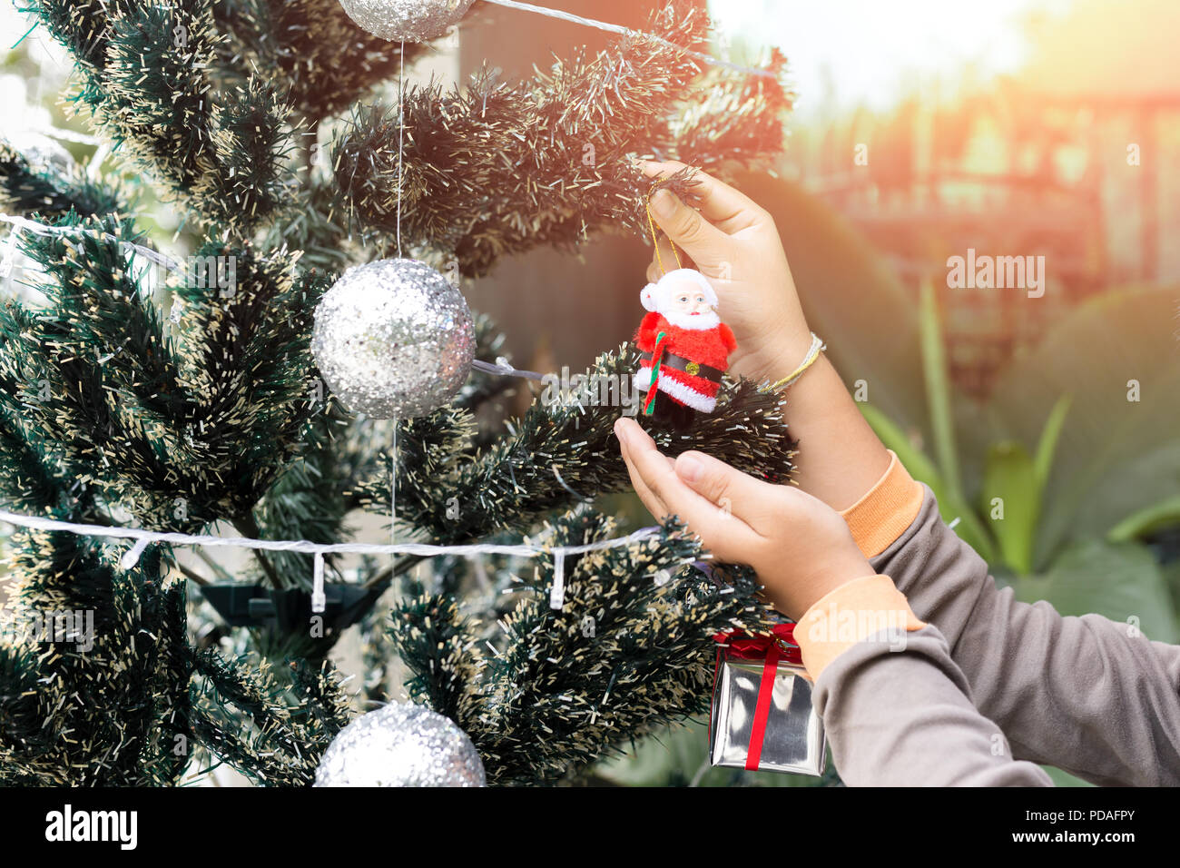 Niñito decora el árbol de Navidad con Santa Claus muñecos de decoración en la luz del sol. Foto de stock