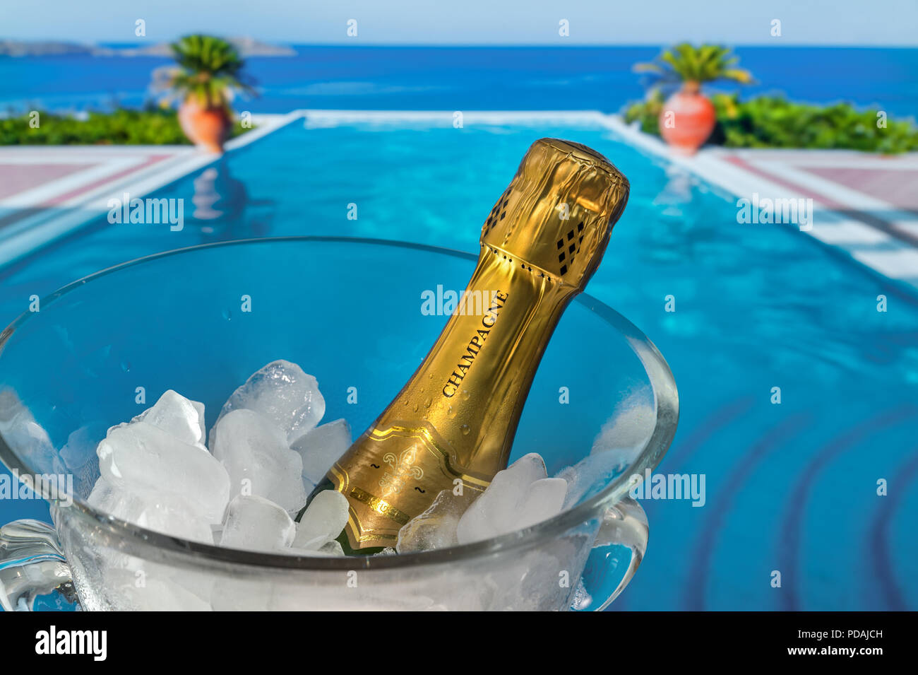 Vacaciones de lujo botella de champán en hielo, escalofriante en vidrio cristal enfriador de vino en la terraza con piscina infinity y vacaciones de lujo en la costa del mar ver detrás Foto de stock