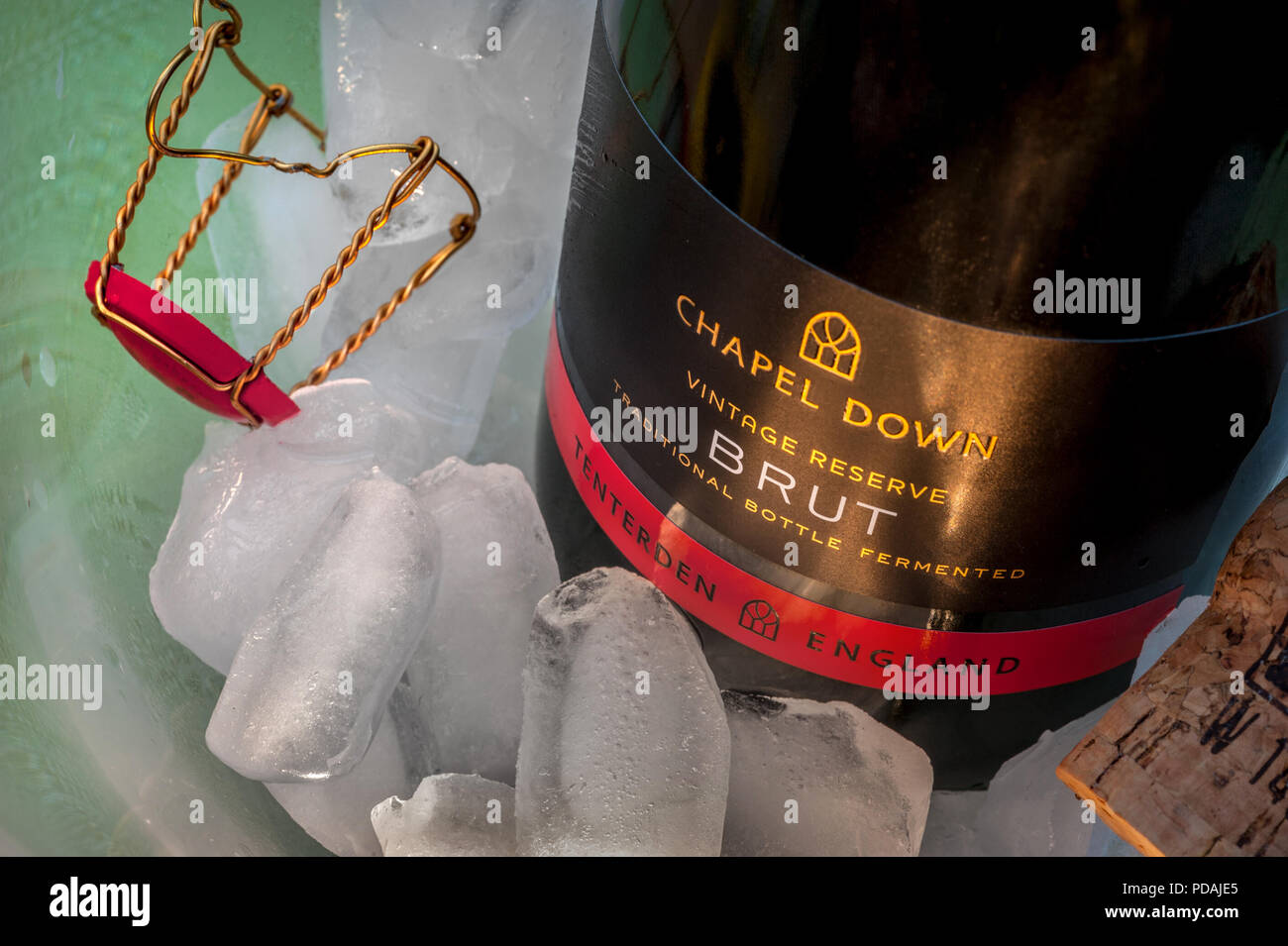 Botella de vino espumoso blanco inglés etiqueta "Capilla abajo Brut' sobre hielo en enfriador de vino, con corcho y tapa retenedora en situación de comedor atmosférica Foto de stock