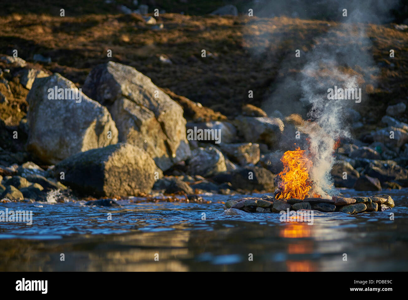 Por Firestack artista Julie Brook.costa oeste de la isla de Lewis. Escocia. Escultura Elemental de Piedra hueca mojón con fuego encendido en una marea entrante Foto de stock
