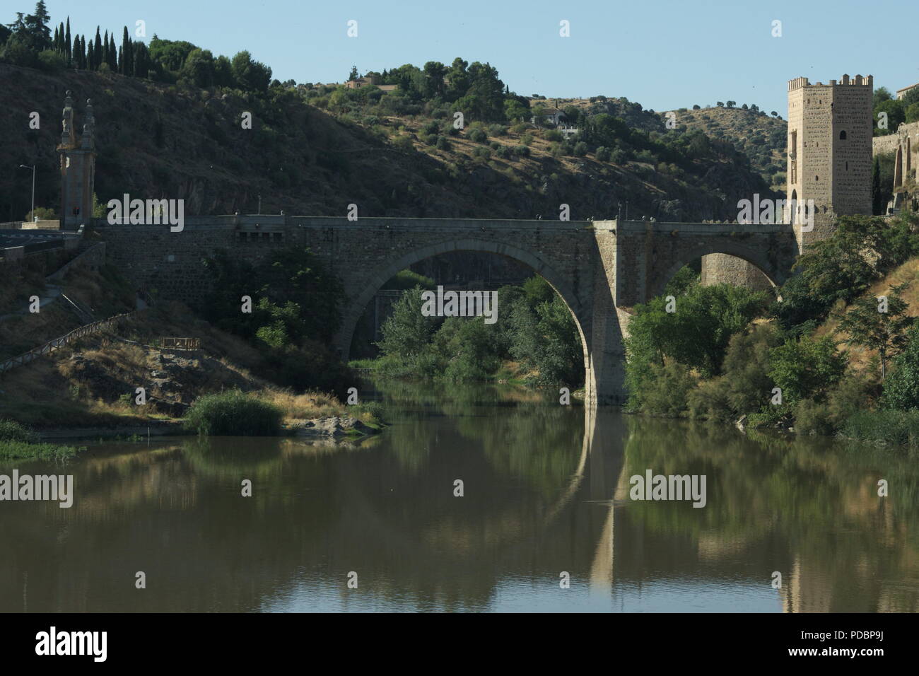 Vista del histórico puente de Alcántara en la antigua ciudad española de Toledo. Una elegante estructura reflejada en las tranquilas aguas del río Tajo. Foto de stock