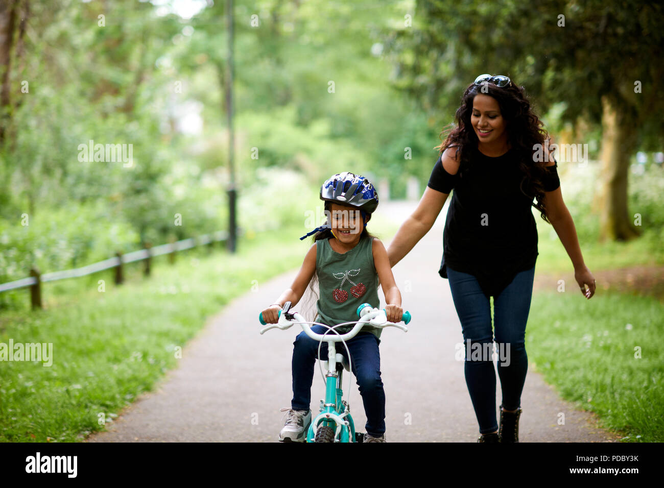 Feliz madre hija enseñando cómo correr en bicicleta Foto de stock