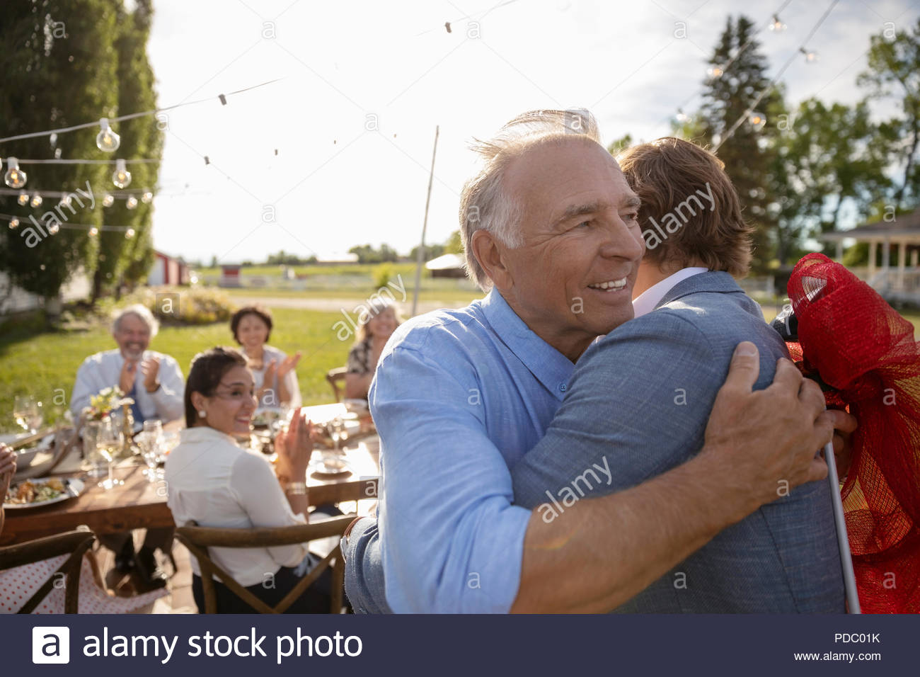 Gracias padre abrazando a hijo en la fiesta de jubilación en jardín rural con amigos Foto de stock
