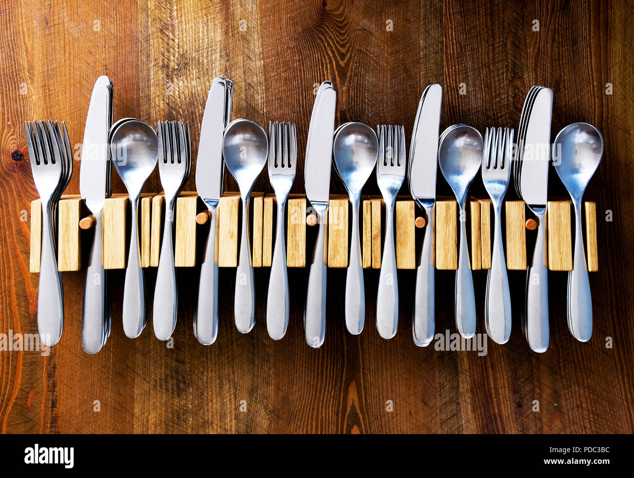 Un montón de cuchillos y tenedores cucharas apostados en una línea de cinco tenedores cubiertos de madera sobre una mesa de madera, fotografía en color Foto de stock