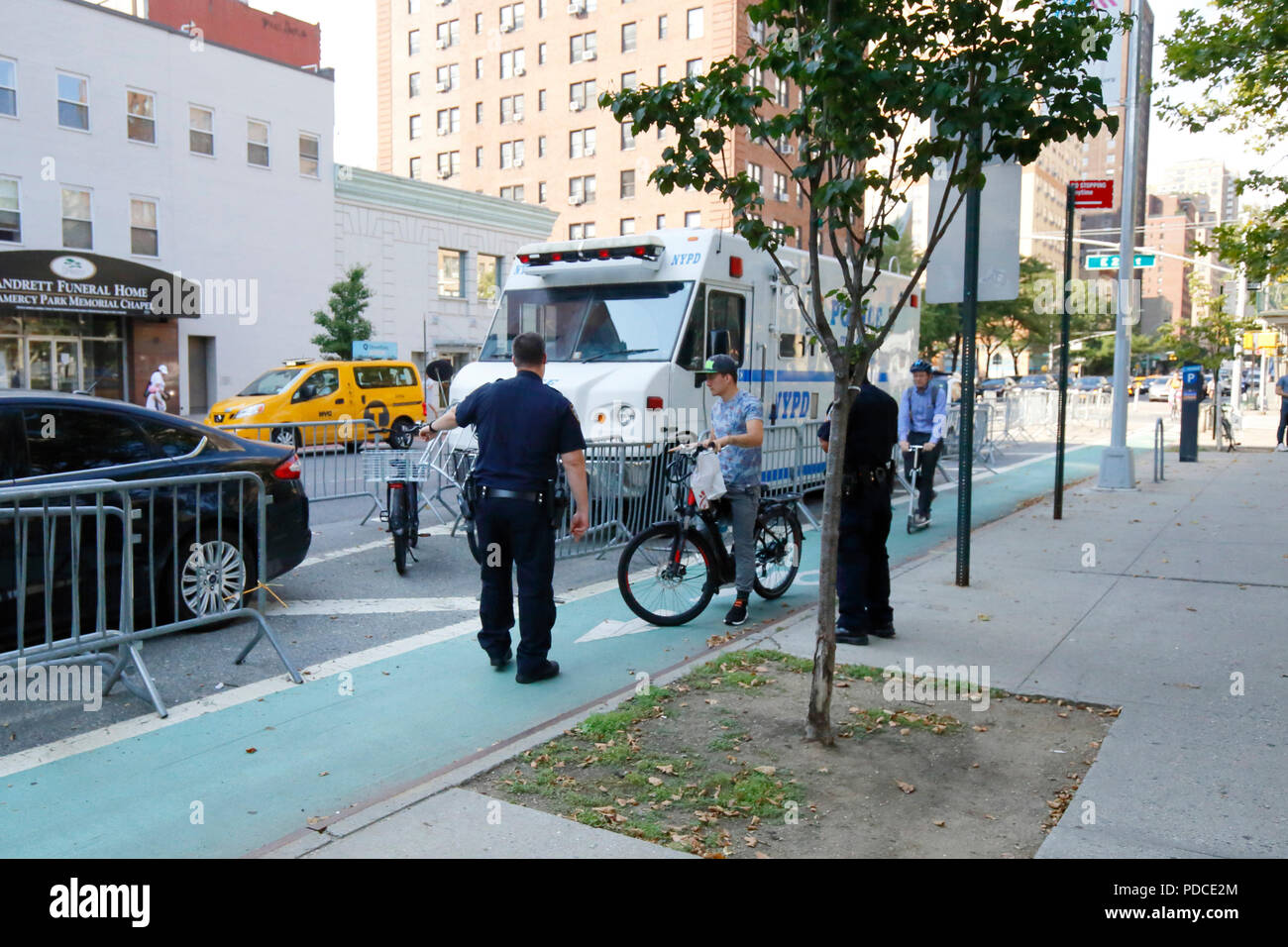 Nueva York, NY, EE.UU. 8 de agosto de 2018. La policía dirige a un ciclista con una bicicleta eléctrica de clase 2 -- asistencia de acelerador -- a una jaula de retención junto al carril bici de la Segunda Avenida en Manhattan. Las bicicletas eléctricas son ilegales en el estado de Nueva York. El alcalde de Blasio de Nueva York ha ordenado al Departamento de Transporte que comience a permitir bicicletas eléctricas asistidas por pedales de clase 1, mientras continúa la ofensiva en todas las bicicletas electrónicas. La mayoría de los usuarios de bicicletas eléctricas son personal de entrega de alimentos. Foto de stock