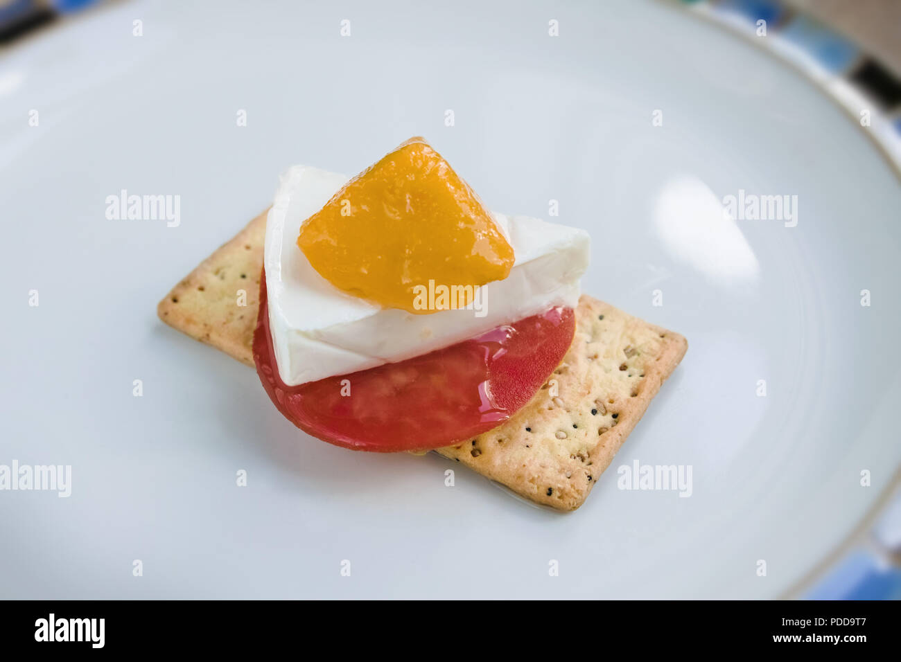 En la placa, en una galleta salada, tenemos una rodaja de tomate, queso, un trozo de mango Foto de stock