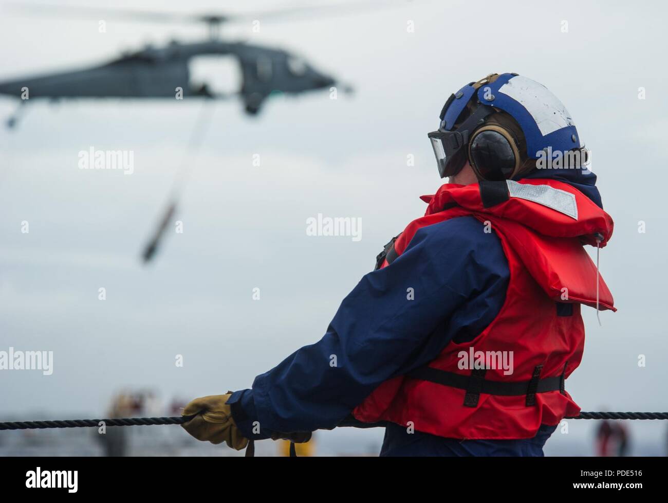 Las aguas al sur de Japón (14 Mayo 2018) marinero Haillie Rotoli mans el teléfono y línea de distancia como un MH-60S Sea Hawk, asignado al comando de Transporte Marítimo Militar (MSC) carga seca/municiones buque USNS César Chávez (T-AKE 14), ofrece detonar en la cubierta de vuelo a bordo de la Marina desplegadas, el portaviones USS Ronald Reagan (CVN 76), como parte de una reposición en alta mar durante las pruebas de mar. Los civiles no combatientes, con tripulación de barco, operado por la MSC, proporciona el combustible, alimentos, municiones, piezas de repuesto, el correo y otros suministros a los buques de la Marina en todo el mundo. Ronald Reagan, el buque insignia de Carrier Strike Group 5 Foto de stock