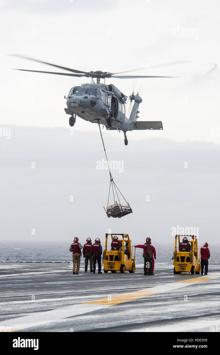 Las aguas al sur de Japón (14 de mayo de 2018) Los marineros de armas departamento espera como un MH-60S Sea Hawk, asignado al comando de Transporte Marítimo Militar (MSC) carga seca/municiones buque USNS César Chávez (T-AKE 14), ofrece detonar en la cubierta de vuelo a bordo de la Marina desplegadas, el portaviones USS Ronald Reagan (CVN 76), como parte de una reposición en alta mar durante las pruebas de mar. Los civiles no combatientes, con tripulación de barco, operado por la MSC, proporciona el combustible, alimentos, municiones, piezas de repuesto, el correo y otros suministros a los buques de la Marina en todo el mundo. Ronald Reagan, el buque insignia de Carrier Strike Group 5, proporciona Foto de stock