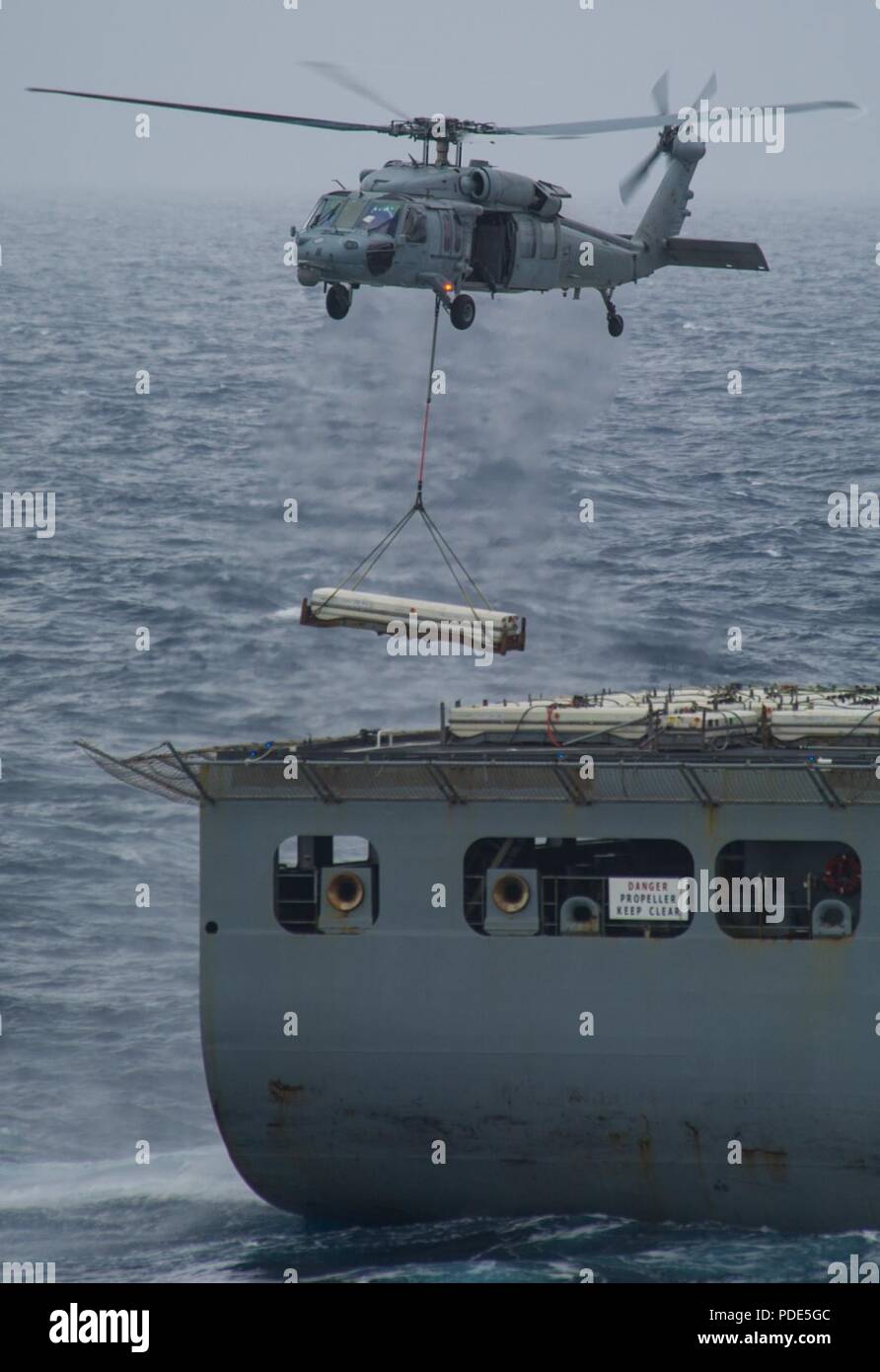 Las aguas al sur de Japón (14 de mayo de 2018) un MH-60S Sea Hawk, asignado al comando de Transporte Marítimo Militar (MSC) carga seca/municiones buque USNS César Chávez (T-AKE 14), suministra explosivos a la Marina desplegadas, el portaviones USS Ronald Reagan (CVN 76), como parte de una reposición en alta mar durante las pruebas de mar. Los civiles no combatientes, con tripulación de barco, operado por la MSC, proporciona el combustible, alimentos, municiones, piezas de repuesto, el correo y otros suministros a los buques de la Marina en todo el mundo. Ronald Reagan, el buque insignia de Carrier Strike Group 5, proporciona listas para combatir la fuerza que protege y defiende el colectivo mari Foto de stock