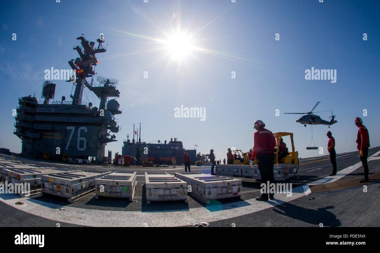 Los marineros estadounidenses mover detonar en la cubierta de vuelo como un MH-60S Sea Hawk helicóptero, asignado al comando de Transporte Marítimo Militar (MSC) carga seca/municiones buque USNS César Chávez (T-AKE 14), Suministra municiones a bordo de la Marina desplegadas en portaaviones USS Ronald Reagan (CVN 76), como parte de una reposición en alta mar durante las pruebas de mar en aguas al sur de Japón, el 15 de mayo de 2018. Los no combatientes civiles, César Chávez, tripulados operados por MSC, proporciona el combustible, alimentos, municiones, piezas de repuesto, el correo y otros suministros a los buques de la Marina en todo el mundo. Ronald Reagan, el buque insignia de Carrier Strike Group 5, pr Foto de stock