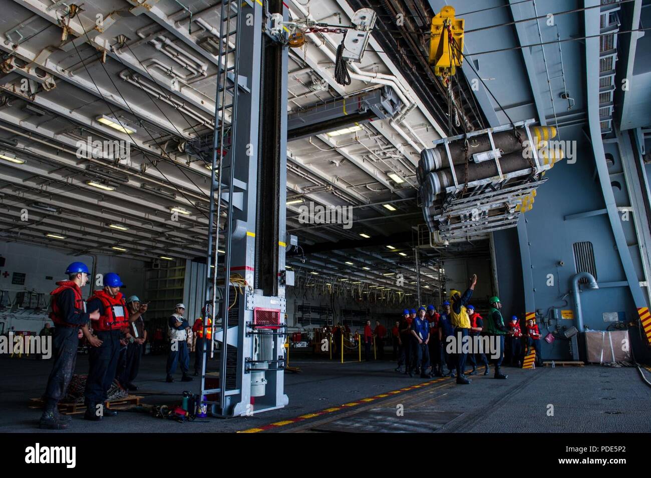 Las aguas al sur de Japón (15 de mayo de 2018) Los marineros de cubierta departamento reciba detonar en el hangar bay a bordo de la Marina desplegadas, el portaviones USS Ronald Reagan (CVN 76), como parte de una reposición en alta mar con el comando de Transporte Marítimo Militar (MSC) carga seca/municiones buque USNS César Chávez (T-AKE 14), durante las pruebas de mar. Los civiles no combatientes, con tripulación de barco, operado por la MSC, proporciona el combustible, alimentos, municiones, piezas de repuesto, el correo y otros suministros a los buques de la Marina en todo el mundo. Ronald Reagan, el buque insignia de Carrier Strike Group 5, proporciona listas para combatir la fuerza que protege y defiende Foto de stock