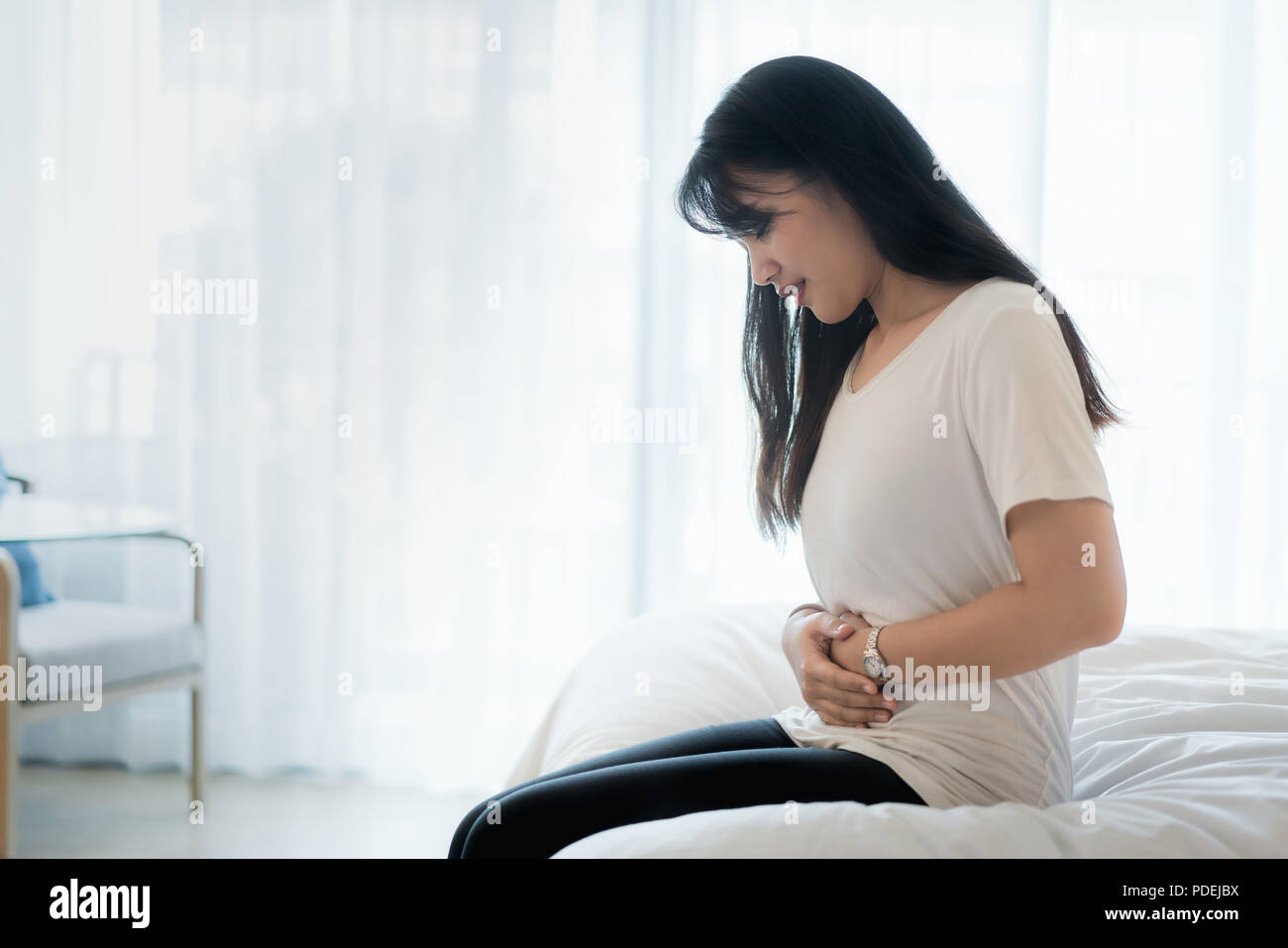 Mujer Asiática de estómago duro en dormitorio, despertar con un dolor de estómago. Foto de stock