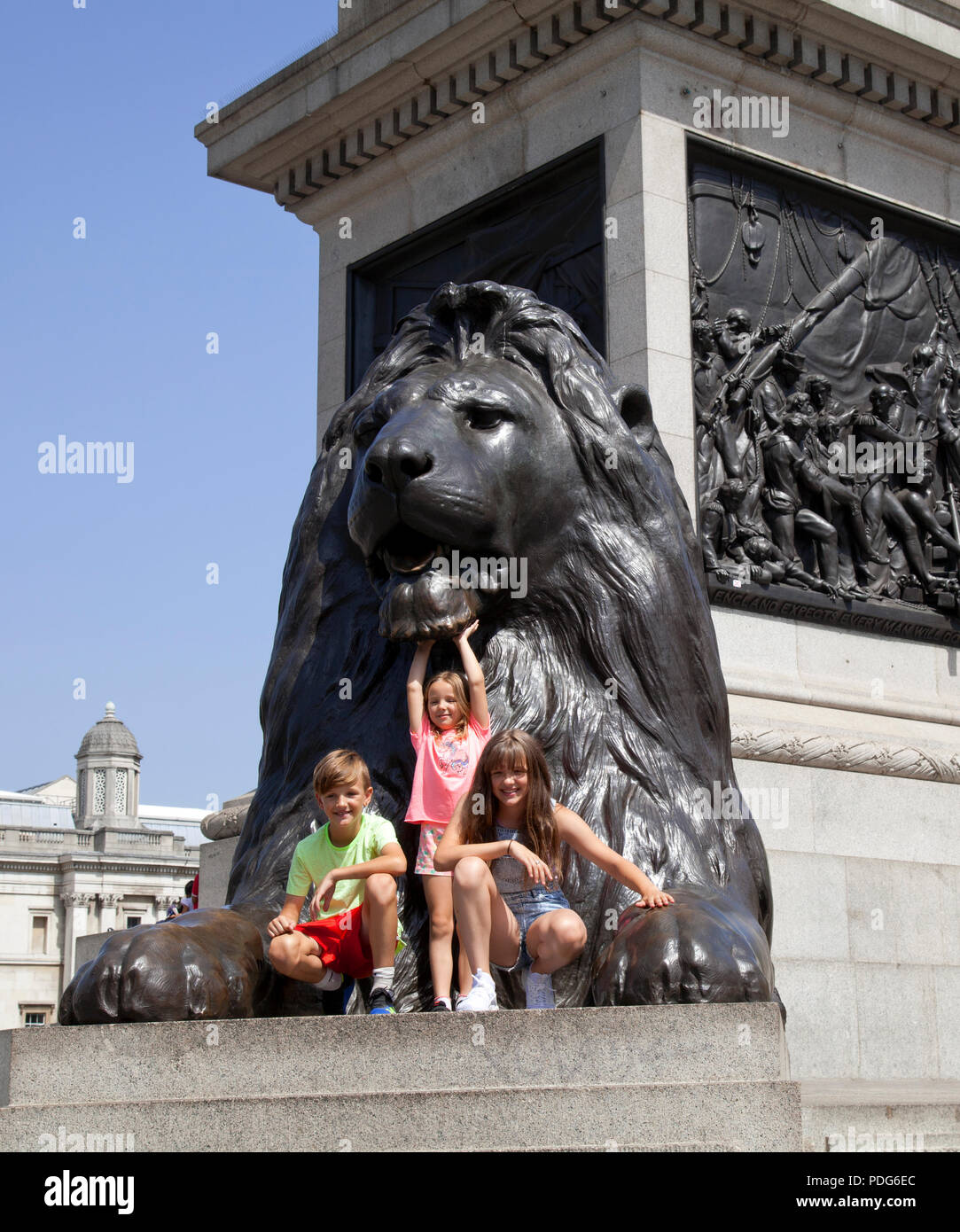 Londres, Trafalgar Square, la base de la columna de Nelson, 2 niñas y un niño posando con león Foto de stock