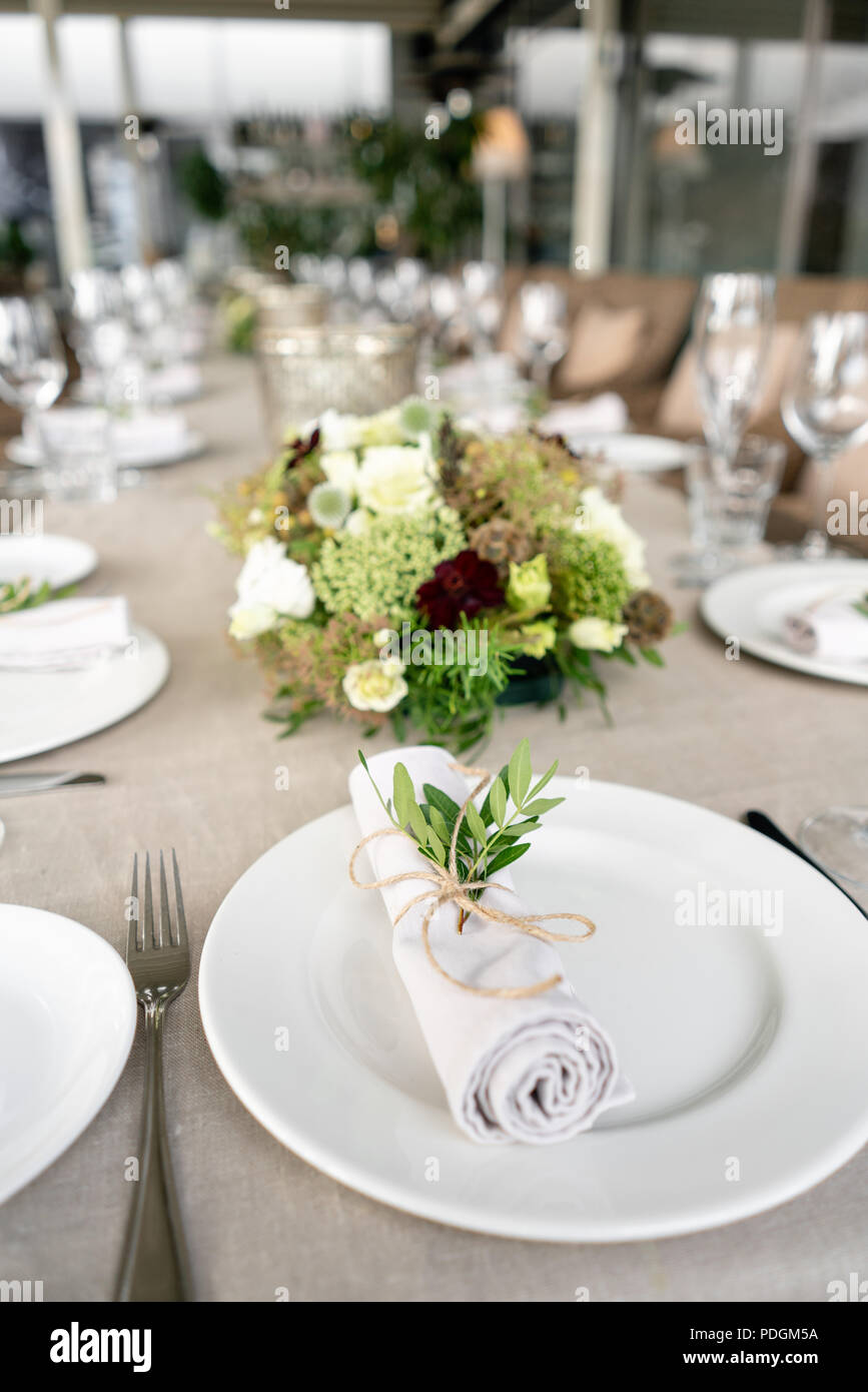 Ordenadamente en un tubo trenzado servilleta comedor decorado con una  ramita de pistacho. Banquete de bodas o cenas de gala. La mesa y sillas  para los huéspedes, servida con vajilla y cubertería.