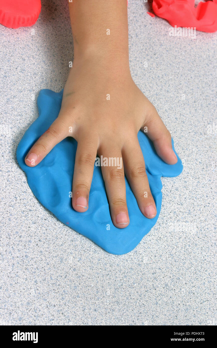 Un niño haciendo una impresión de mano en algunas suave maleable plastilina azul Foto de stock