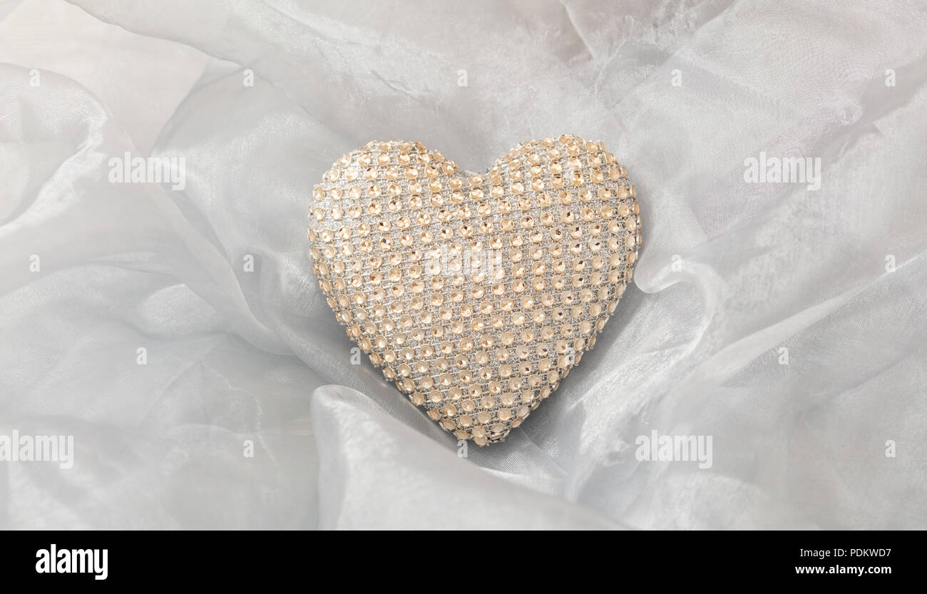 Amor y matrimonio concepto. Golden sequin corazón, vista superior en un tul de seda blanca de fondo. Foto de stock