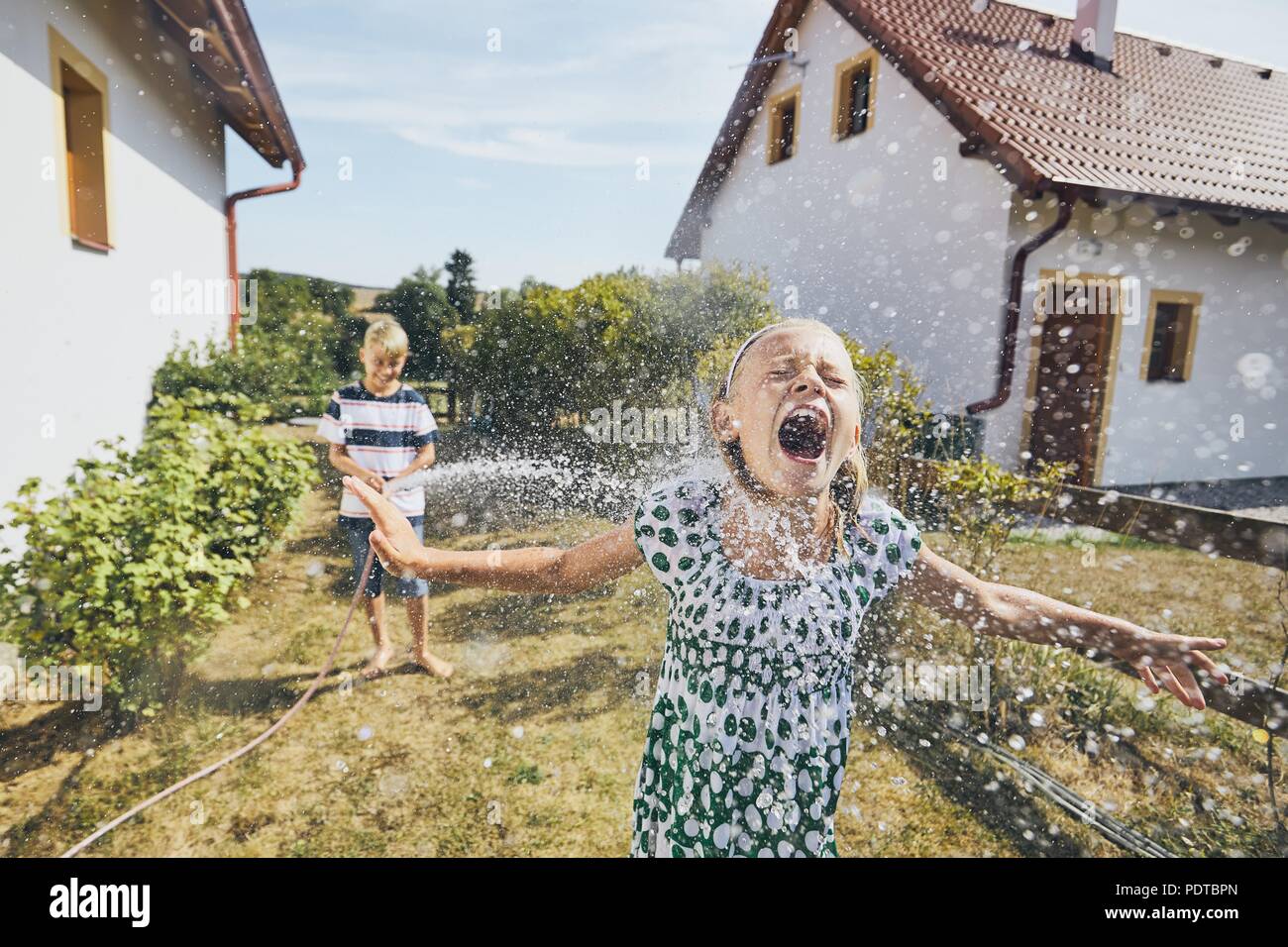 Los niños se divierten con las salpicaduras de agua. Hermanos en el patio trasero de la casa durante el día de verano. Foto de stock