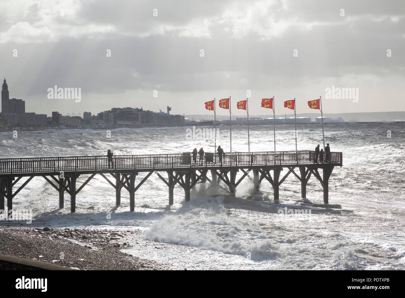 Olas y surf rompiendo en tierra en una tormenta invernal en Sainte Adresse, Le Havre, Normandía, Francia, con la silueta del muelle en primer plano Foto de stock